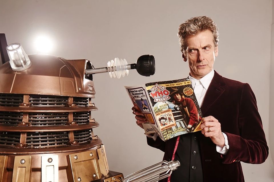 Peter Capaldi in costume as the Doctor reading the inaugural issue of Doctor Who Weekly to a Dalek
